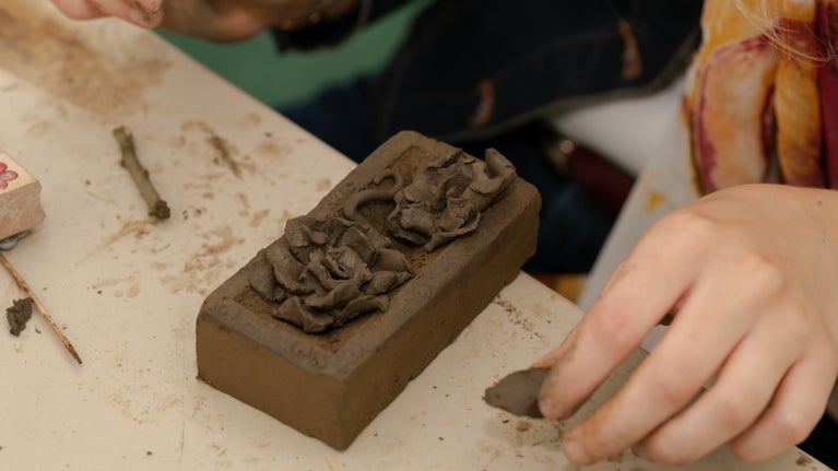 A brick on a workbench with additional decorations shaped like tentacles and bubbles in the same dark material. A person's hands are ready to add the next decoration.